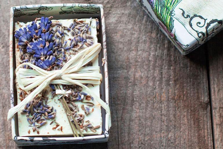 A bar of lavender soap in a fancy decorative box with twine tied around it and some of the lavender plant pressed and tied together with the bar of soap.