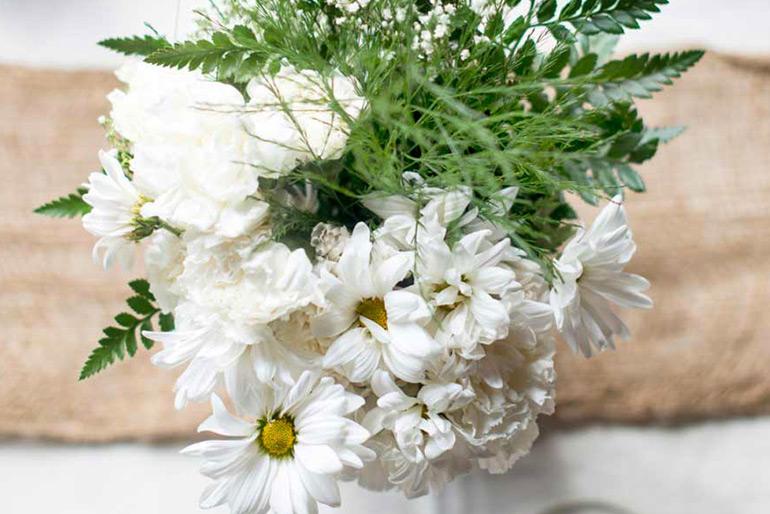 A bouquet of flowers including daisies and a type of fern all within a vase that is not visible in the photo as the flowers completely cover it.