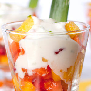 This is a short, wide glass with Mexican Fruit Cocktail With Sweet Lime Yoghurt. This fruit cocktail contains papaya, mango, pineapple, and pomegranate seeds. The sweet lime yogurt topping contains Mountain High Plain Yoghurt, coconut milk, honey, and lime.